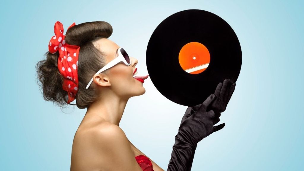 The side profile of a young, pretty woman licking a record that she's holding in her gloved hands