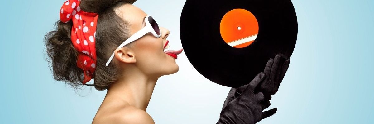 The side profile of a young, pretty woman licking a record that she's holding in her gloved hands