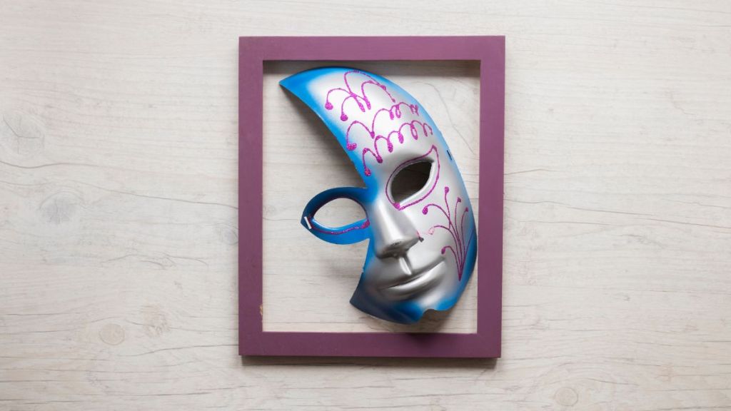 A cut out silver face mask missing half a forehead and cheek framed in a purple colored frame