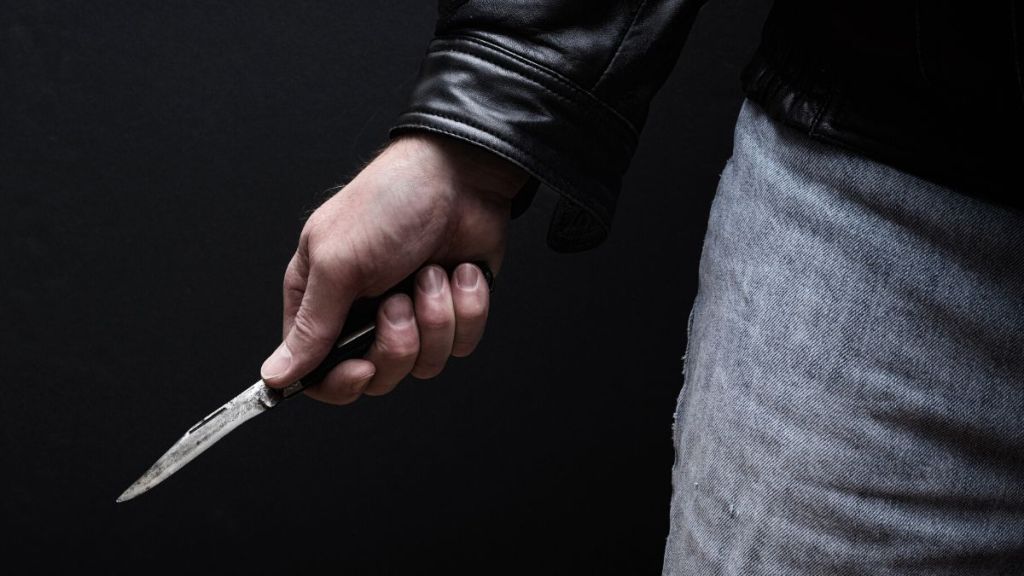 A close up of a man's hand near his thigh and holding a knife