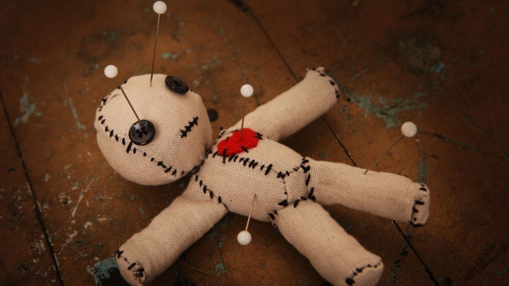 A small jute doll with a red heart and voodoo pins sticking out of it